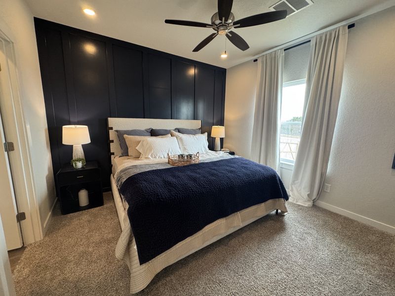 A cozy bedroom featuring a dark accent wall, elegant bedding, and soft carpeted flooring complete with warm bedside lighting. A cozy bedroom featuring a dark accent wall, elegant bedding, and soft carpeted flooring complete with warm bedside lighting.