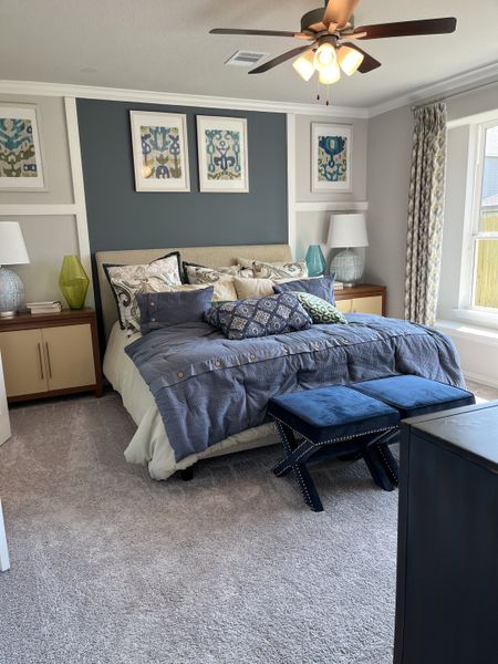 A cozy bedroom featuring a plush bed, textured blue accents, abstract art, and elegant furnishings under a warm ceiling fan. A cozy bedroom featuring a plush bed, textured blue accents, abstract art, and elegant furnishings under a warm ceiling fan.