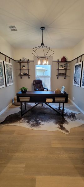 A modern home office with a sleek black desk, leather chair, geometric light fixture, and stylish shelving.