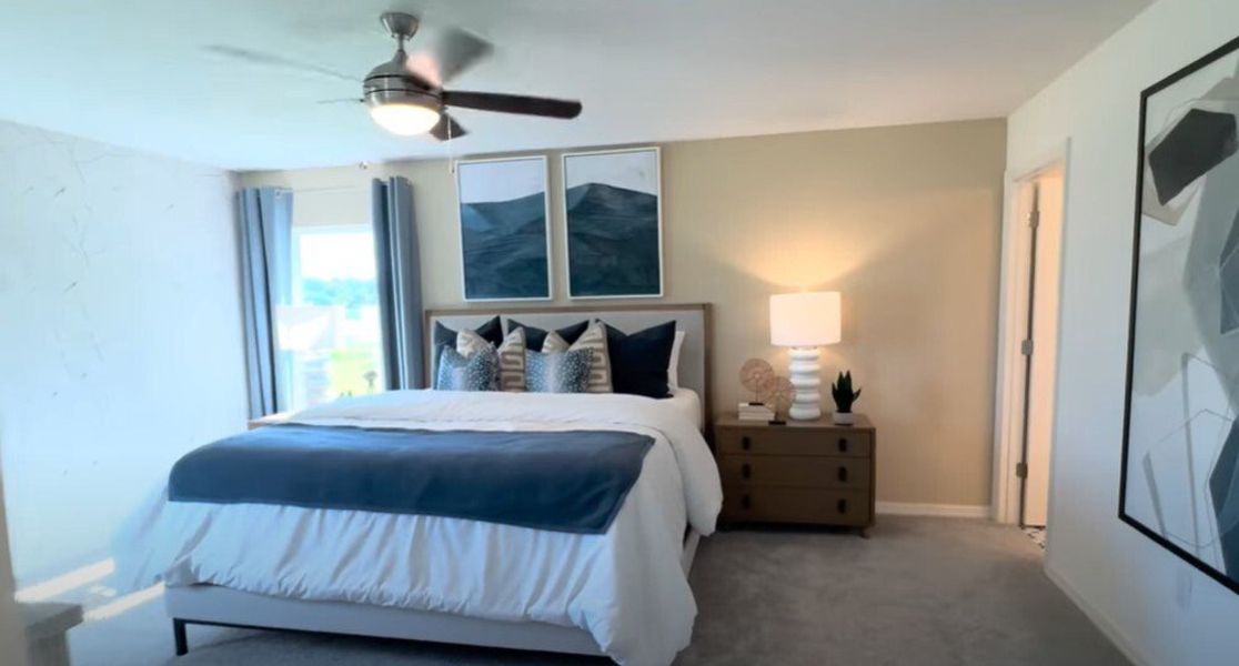 A cozy bedroom featuring a plush bed with blue accents, modern artwork, and warm lighting creating a serene retreat.