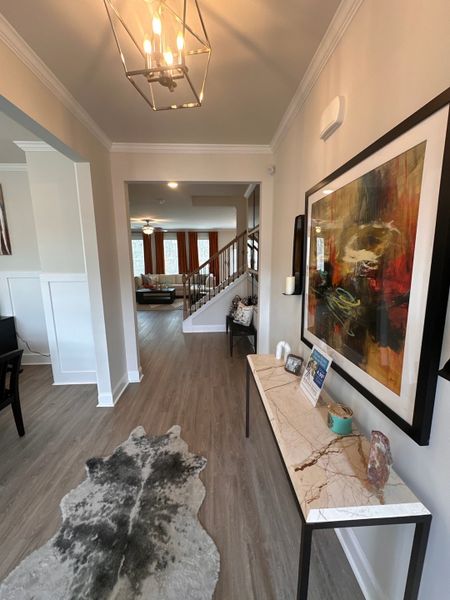 A welcoming hallway with modern lighting, abstract art, a sleek console, and wooden flooring leading to a cozy living space.