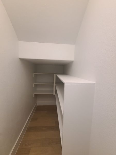 A compact, angled closet with white shelving and light wood flooring, providing efficient storage space.