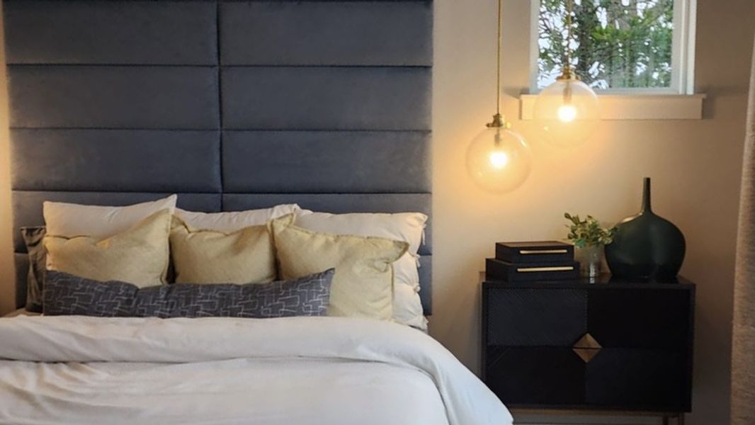 A modern bedroom with a striking blue upholstered headboard, pendant lighting, and warm wood flooring for a cozy and stylish retreat.
