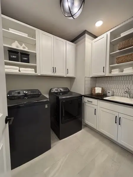 A modern laundry room with sleek black appliances, ample cabinetry, and stylish tile accents in Eden at Crossprairie by M/I Homes (St. Cloud, FL).