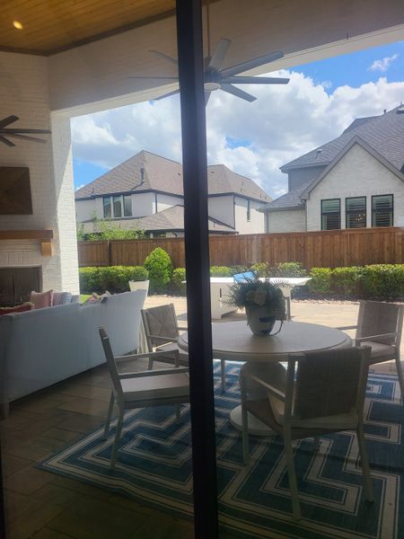 A stylish outdoor patio featuring a chic dining set, plush seating, and a cozy fireplace under a wooden ceiling with fans.