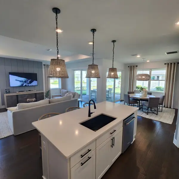 Open-concept living area with chic pendant lights, sleek island, and bright dining space leading to a cozy patio.