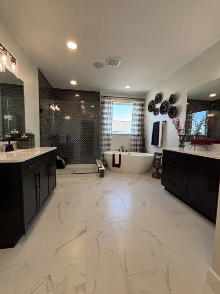 A stylish bathroom featuring a blue accent wall, a classic white vanity, and a tiled bathtub in Eden at Crossprairie by M/I Homes (St. Cloud, FL).