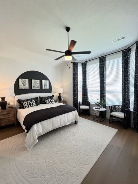 A modern bedroom with a bold black accent wall, elegant bedding, and large windows framed by patterned drapes. A modern bedroom with a bold black accent wall, elegant bedding, and large windows framed by patterned drapes.