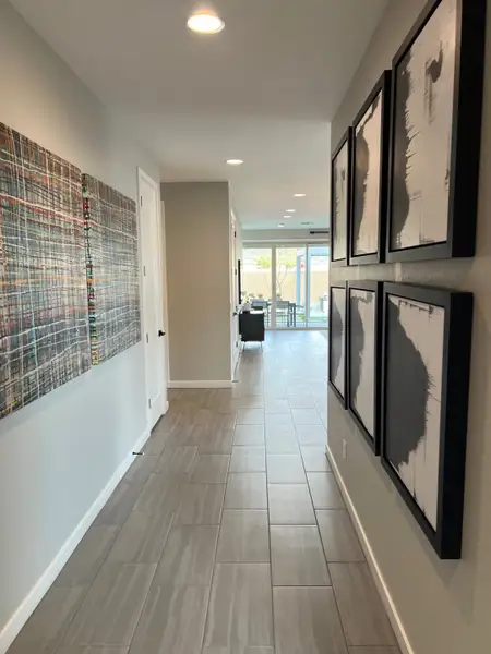 A modern hallway with sleek tiled flooring, contemporary art pieces, and recessed lighting leading to a bright living area.