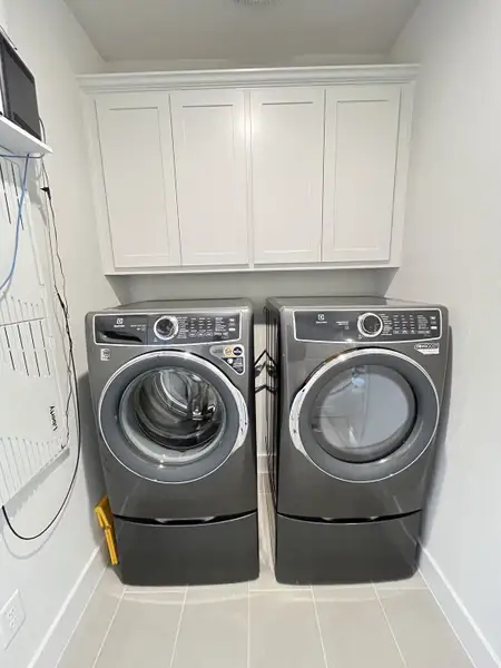 A modern laundry room with sleek gray washer and dryer set, white cabinetry, and tile flooring. A modern laundry room with sleek gray washer and dryer set, white cabinetry, and tile flooring.