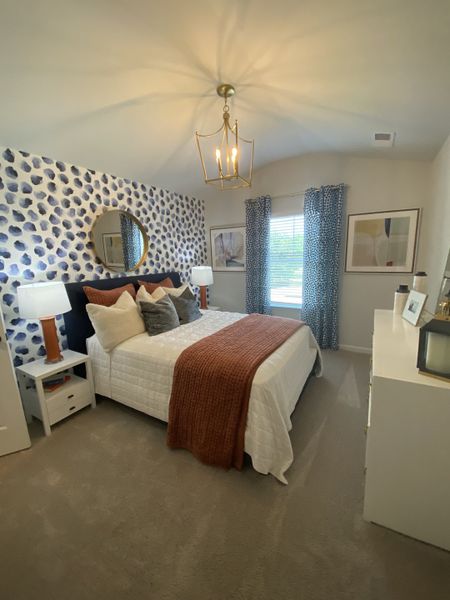 A cozy bedroom with a patterned accent wall, elegant light fixture, and inviting bed with textured pillows and throw.