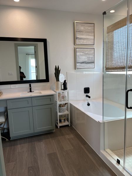A modern bathroom with a sleek vanity, wood flooring, glass shower, and elegant decor.
