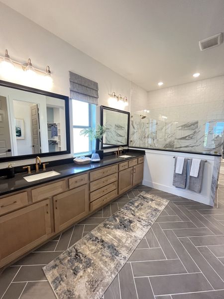 A modern bathroom featuring dual sinks, dark countertops, a spacious shower, and elegant lighting with herringbone flooring. A modern bathroom featuring dual sinks, dark countertops, a spacious shower, and elegant lighting with herringbone flooring.
