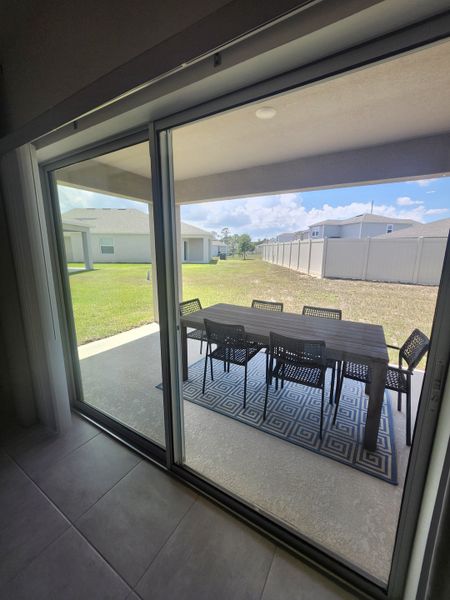 A patio view with sliding glass doors, featuring an outdoor dining set on a patterned rug, and a neatly mowed lawn.