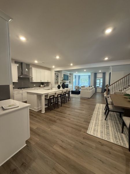 An open-concept kitchen and living area with wood flooring, bright lighting, and elegant dining space.