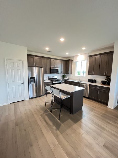 Modern kitchen with sleek dark cabinets, stainless steel appliances, and a central island with seating on wood floors. Modern kitchen with sleek dark cabinets, stainless steel appliances, and a central island with seating on wood floors.