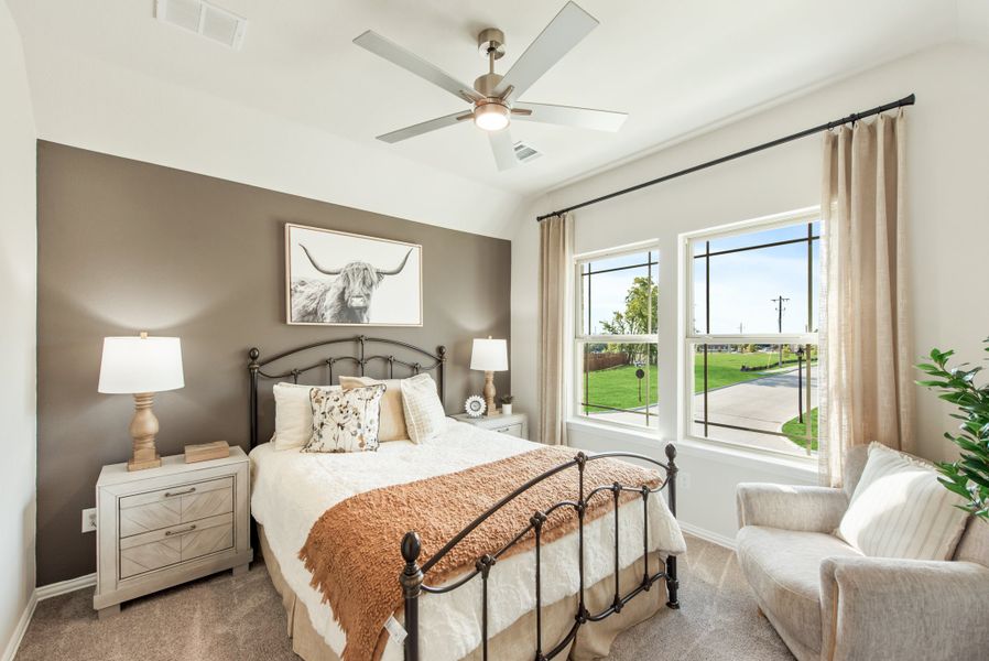 Bedroom with iron bed frame, dark accent wall, ceiling fan, and two windows with neutral curtains