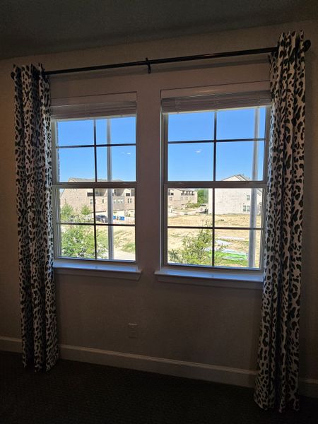 A room with large windows framed by patterned curtains, providing a bright view of the outdoors.