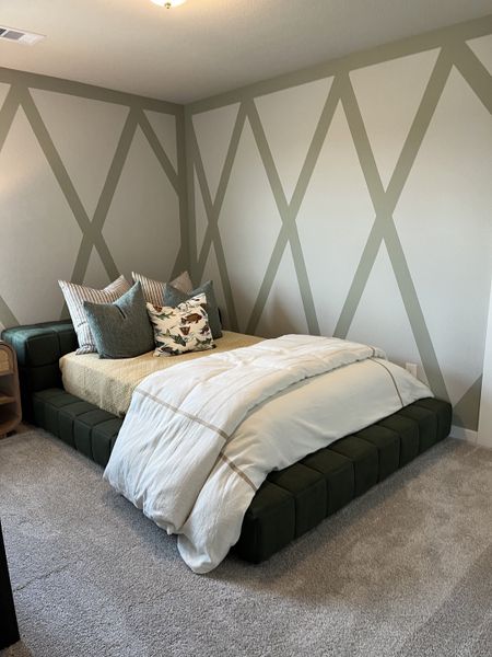 A cozy bedroom features geometric wall patterns, plush carpeting, and an inviting bed with soft, layered bedding.