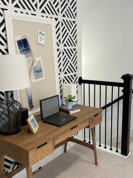A stylish home office with a wooden desk, laptop, patterned accent wall, and modern decor.