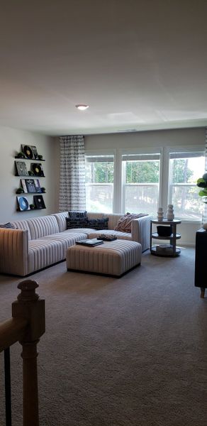 A cozy living room with a striped sectional sofa, album wall decor, and large bright windows.