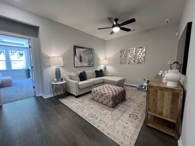 A cozy living area with a sectional sofa, tufted ottoman, and stylish decor, featuring soft lighting and elegant accents.