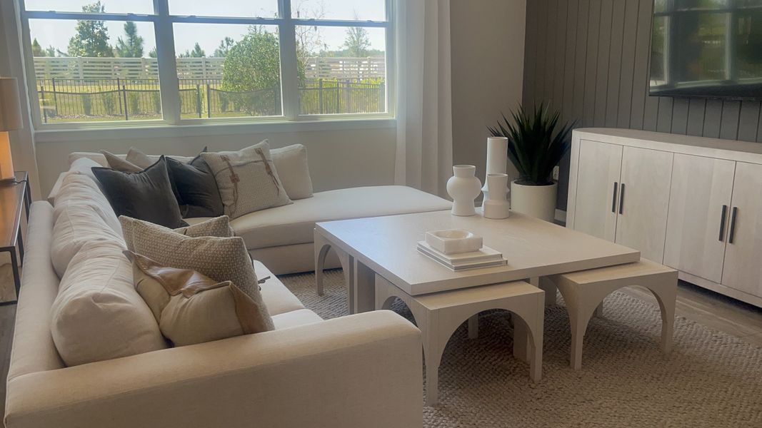 A cozy living room with a beige sectional, soft pillows, modern decor, and natural light from a large window. A cozy living room with a beige sectional, soft pillows, modern decor, and natural light from a large window.