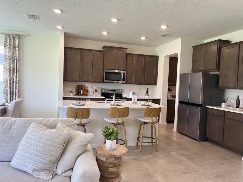 A modern kitchen features wooden cabinets, stainless steel appliances, and a cozy breakfast bar with stylish bar stools.