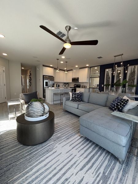 A sophisticated living room with a coffered ceiling, stylish lighting, and plush seating in Eden at Crossprairie by M/I Homes (St. Cloud, FL).