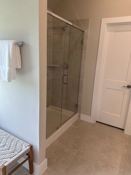 A modern bathroom featuring a glass-enclosed shower, sleek tile flooring, and a woven bench accent. A modern bathroom featuring a glass-enclosed shower, sleek tile flooring, and a woven bench accent.