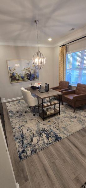 A cozy home office with elegant lighting, a modern desk, plush chairs, and an abstract rug for a sophisticated feel.