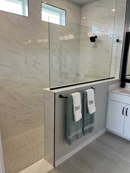 A sleek shower area with marble-style tiles, glass enclosure, and modern fixtures, accented by plush towels on a matte black rack.