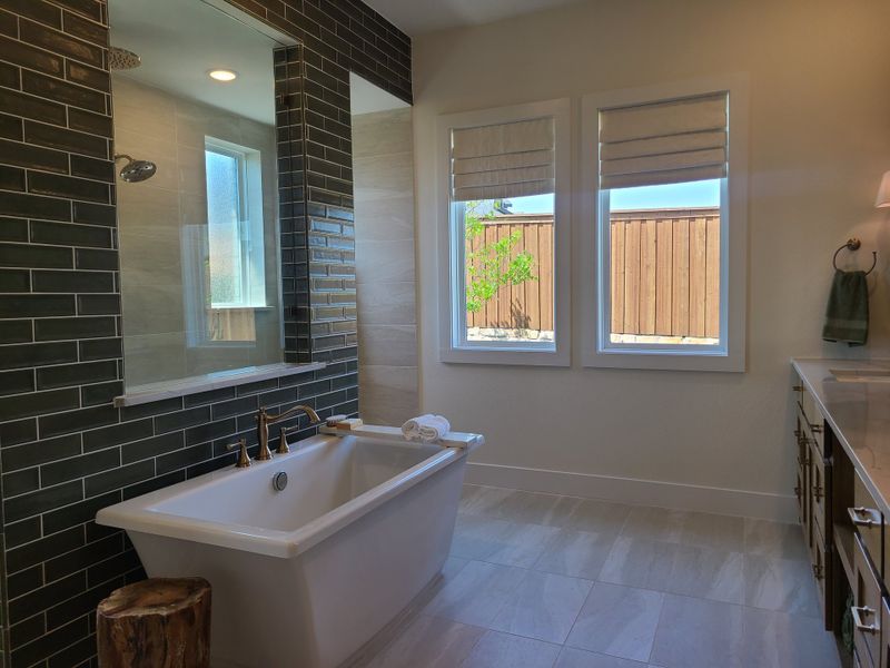 A modern bathroom with a sleek white tub, dark subway tiles, dual windows, and elegant fixtures.