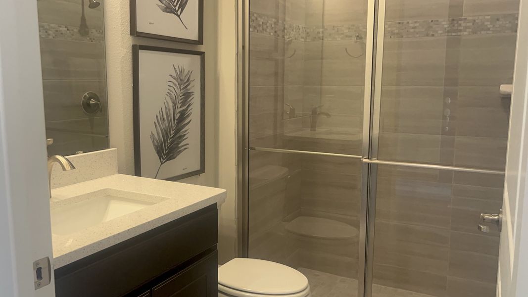 A modern bathroom with tiled shower, glass doors, sleek vanity, and framed botanical art.