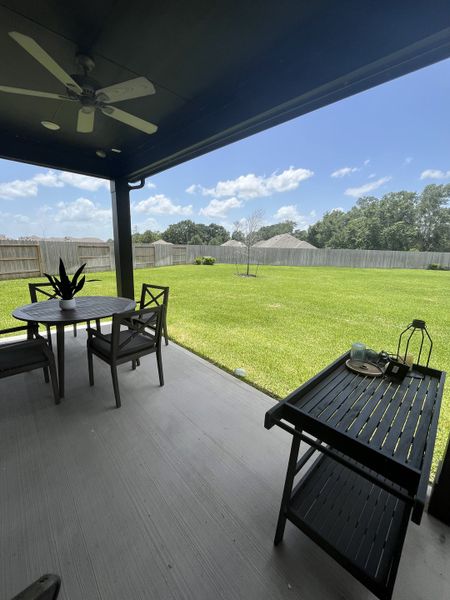 A covered patio with a ceiling fan overlooks a spacious, grassy backyard, perfect for outdoor dining and relaxation. A covered patio with a ceiling fan overlooks a spacious, grassy backyard, perfect for outdoor dining and relaxation.