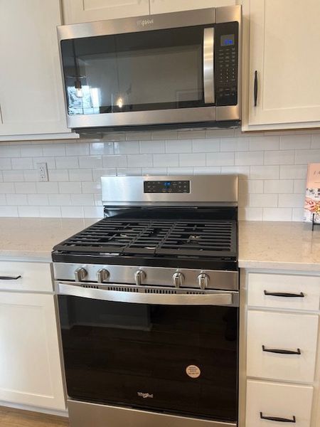 Modern kitchen featuring stainless steel appliances, white cabinetry, and a sleek subway tile backsplash.