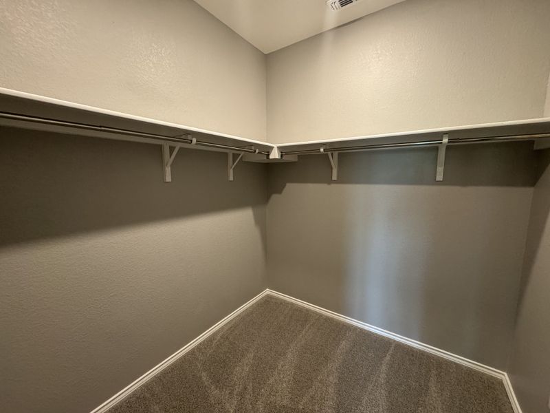 A spacious walk-in closet with neutral walls, shelving, and ample hanging space.