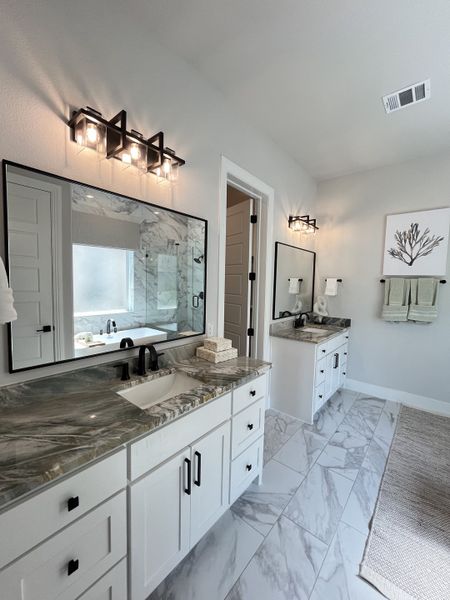 A luxurious bathroom with marble countertops, sleek double sinks, and elegant lighting on a tiled floor.