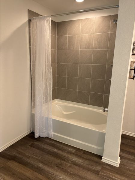 A modern bathroom featuring a sleek bathtub with gray tile surround and warm wood flooring.