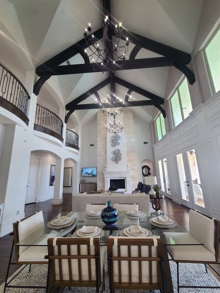 An elegant living room with vaulted ceilings, exposed beams, chandeliers, and a stylish dining area featuring a glass table. An elegant living room with vaulted ceilings, exposed beams, chandeliers, and a stylish dining area featuring a glass table.