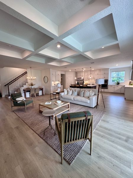 An elegant open-concept living area with coffered ceilings, cozy seating, and a modern kitchen.