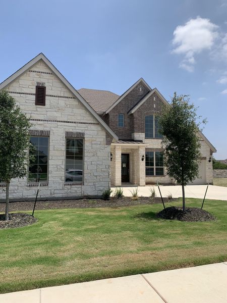 A beautiful stone and brick home with manicured landscaping in Oaks at San Gabriel by Brightland Homes (Georgetown, TX).