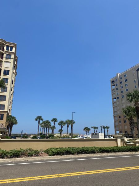 Elegant beachfront buildings and palm trees under a clear sky in Townhomes on 1st by Benchmark Commercial Group (Jacksonville Beach, FL).