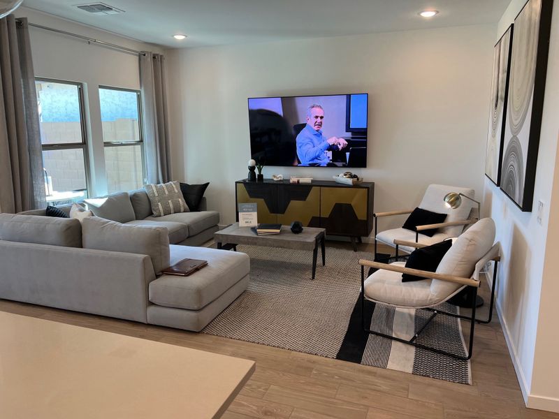 A modern living room with a cozy gray sectional, sleek armchairs, and a large TV. Neutral tones and stylish decor accents.