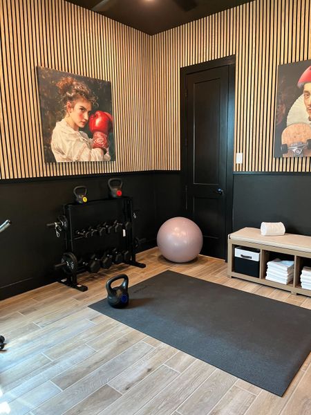 A stylish home gym with wood flooring, striped walls, workout equipment, and artistic decor.
