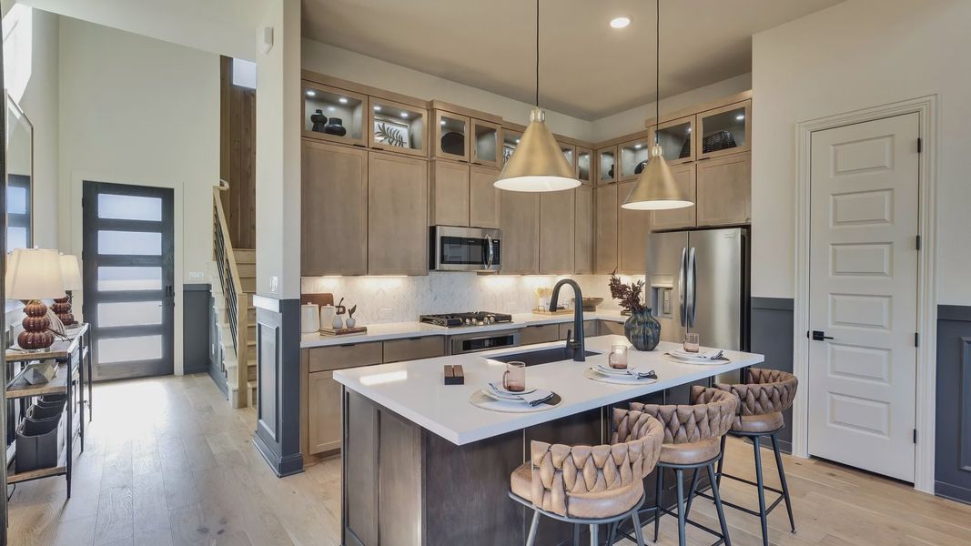 Elegant wooden cabinetry and sleek island elevate this Flora community kitchen in Texas to opulent heights.