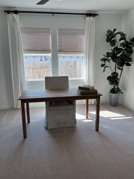 A bright home office with a wooden desk, cozy chair, and large windows draped with white curtains. A bright home office with a wooden desk, cozy chair, and large windows draped with white curtains.