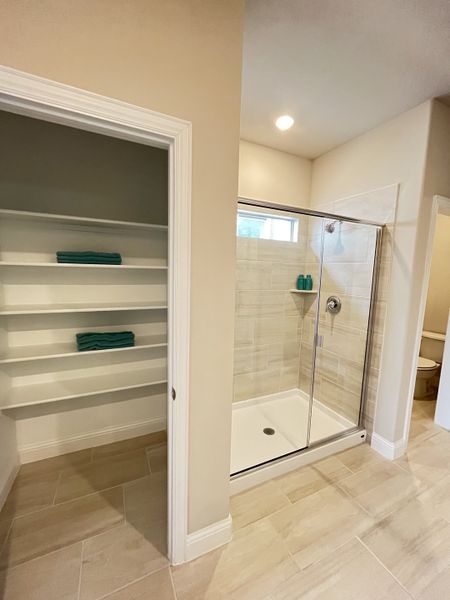 A modern bathroom with glass shower doors, beige tiles, open shelving, and recessed lighting.