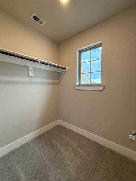 A cozy walk-in closet with soft carpet, a wooden shelf, and a window allowing natural light.