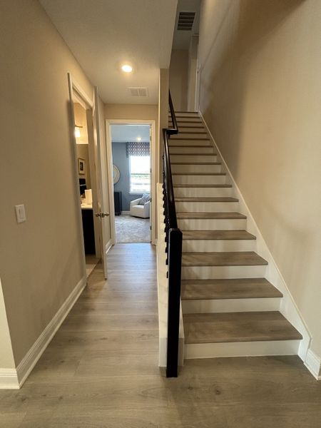 A warm and inviting hallway with wood-look flooring, elegant lighting fixtures, and soft beige walls, creating a welcoming entrance in Crossroads at Kelly Park by Dream Finders Homes (Apopka, FL).